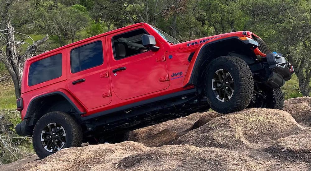 A red 2024 Jeep Wrangler Rubicon is shown driving over rocks after visiting a Jeep dealer.