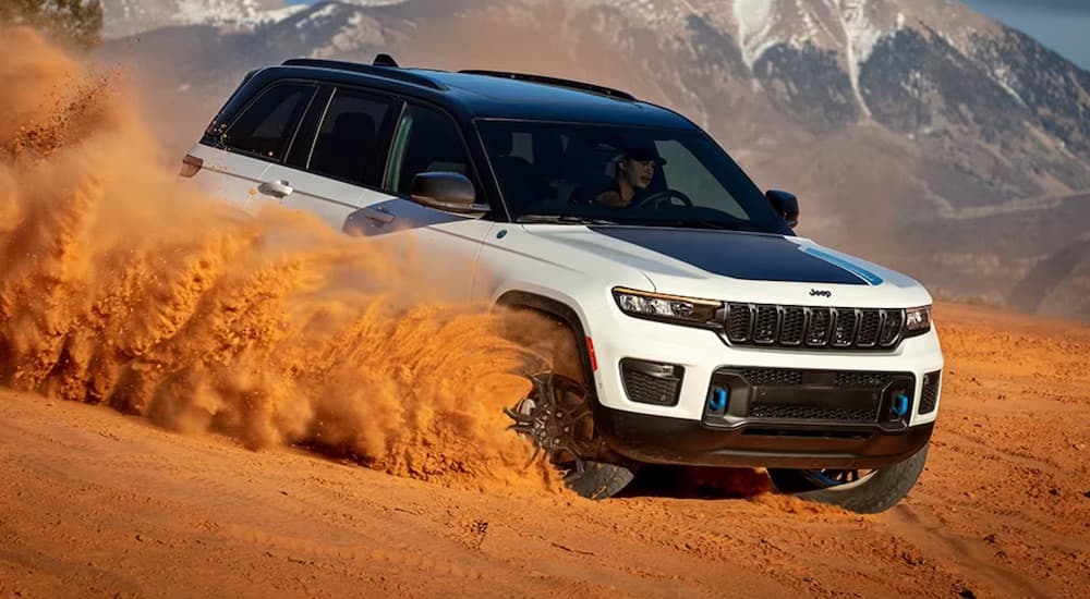 A white and black 2024 Jeep Grand Cherokee 4xe is shown driving down a sandy hill.